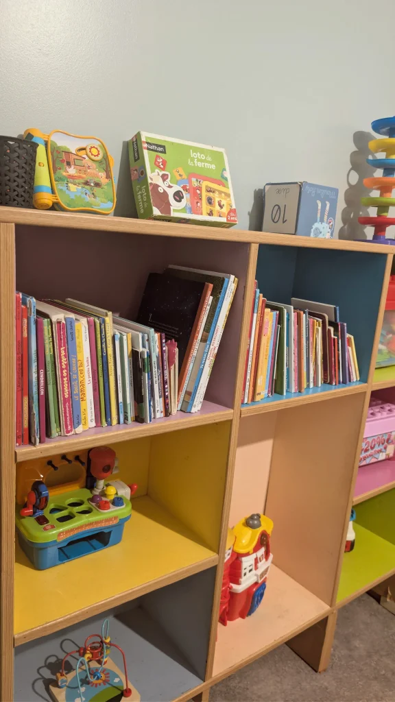 Détail des livres et jeux d'éveil (loto de la ferme, boulier) sur une étagère colorée à la MAM Les Chérubins à Perpignan