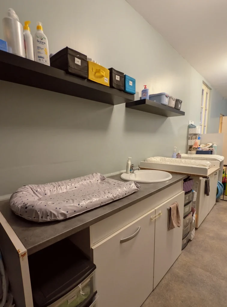 Espace de change et nursing propre et organisé de la MAM Les Chérubins à Perpignan, comprenant plusieurs tables à langer, un point d'eau et des rangements pour les soins des enfants.