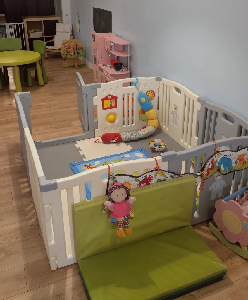 Espace d'éveil sécurisé pour bébés à la MAM Les Chérubins à Perpignan, avec tapis en mousse, parcours de motricité souple, tunnel et jouets sensoriels suspendus.