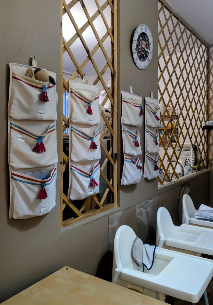 Porte-doudous individuels en tissu accrochés au mur de la MAM Les Chérubins à Perpignan, montrant un environnement organisé et respectueux du rythme de l'enfant.